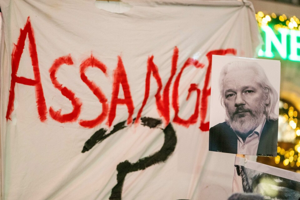 Plakater med bilde av Julian Asange i en lysmarkering og tog i forbindelse med fredsprisen 2021. Assange er flere ganger nevnt som en fredspriskandidat. Bildet er av et banner der det står Assange i rødt. Det er et bilde av ham festet på banneret. Han har på skjorte og jakke. Han har bølgete hvitt hår til nakken og helskjegg. Foto: Terje Pedersen / NTB
