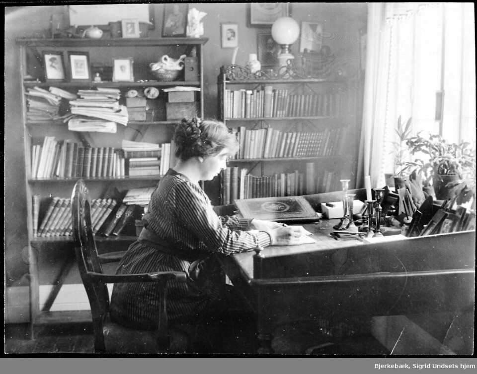 Sigrid Undset sitter ved skrivebordet i Røssumstua, 1920-1922. Sigrid Undset sitter ved skrivebordet i Røssumstua, 1920-1922.