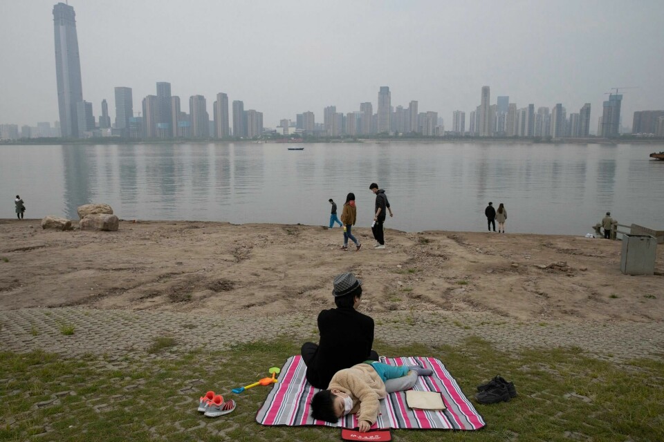 Et barn sover ved siden av Yangtze-elven, i millionbyen Wuhan i Kina. Det er i denne byen det første kjente koronautbruddet i verden oppsto. A child wearing a face mask takes a nap along the Yangtze River in Wuhan in central China's Hubei province on April 5, 2020. (AP Photo/Ng Han Guan)