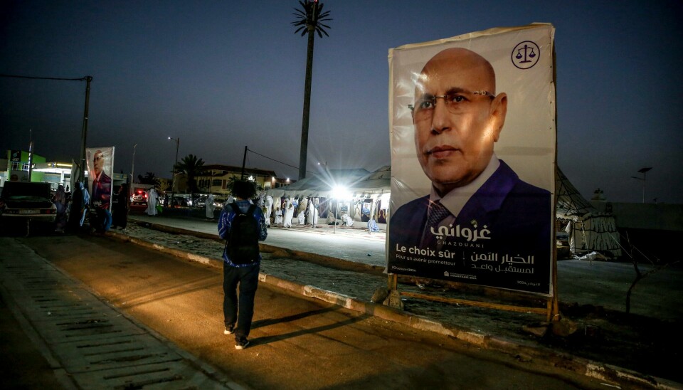 En mann går forbi en valgplakat i Nouakchott som viser president Mohamed Ould Ghazouani. Det har brutt ut uro i Mauritanias hovedstad etter at det ble klart at Ghazouani får, en ny presidentperiode. «Trygt valg» står det på plakaten til president Mohamed Ould Cheikh El Ghazouani. Den sittende presidenten får tilliten i en ny periode. Foto: Mamsy Elkeihel / AP / NTB