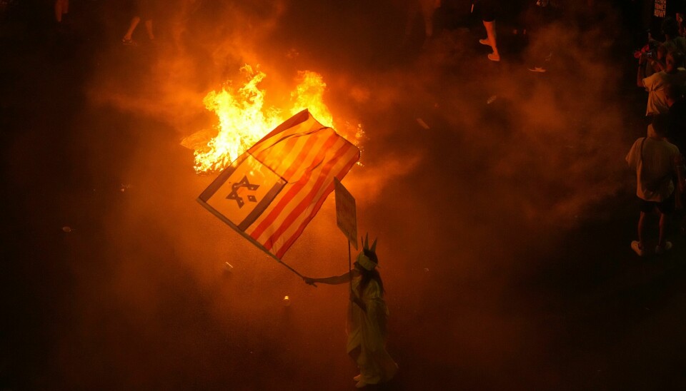 En demonstrant med israelsk-amerikansk flagg under demonstrasjonen i Tel Aviv lørdag kveld. En demonstrant med israelsk-amerikansk flagg under demonstrasjonen i Tel Aviv lørdag kveld. Foto: Ariel Schalit / AP / NTB