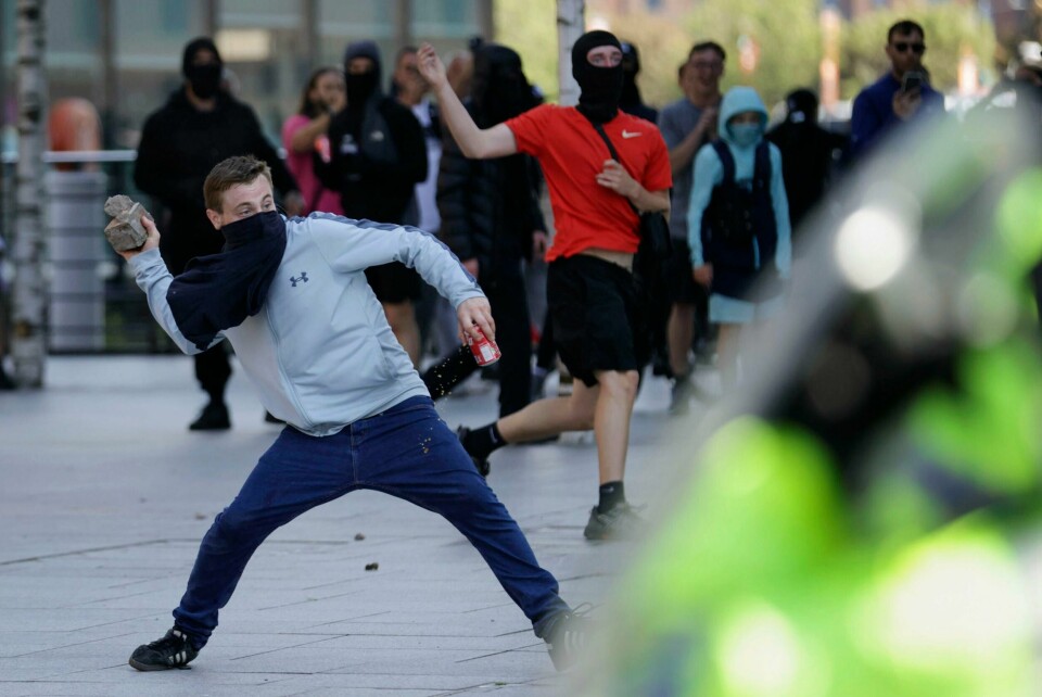 En demonstrant kaster murstein i Liverpool lørdag. Flere politifolk er skadet i opptøyene i byen. En demonstrant kaster murstein i Liverpool lørdag. Flere politifolk er skadet i opptøyene i byen. Foto: James Speakman / AP / NTB