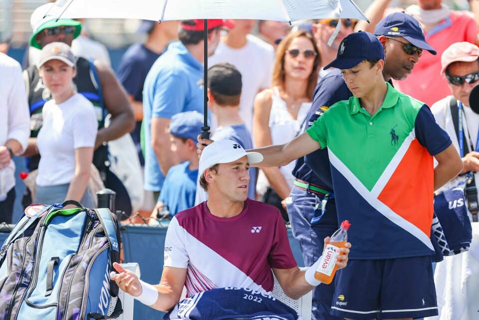 Casper Ruud og resten av tenniseliten er vant til høye temperaturer og lange styrkeprøver. Her tar Ruud en pause i skyggen i US Open i fjor. Tirsdag er det meldt enda varmere enn det var i New York i august. Casper Ruud tar en hvil i skyggen fra en paraply under matchen mot britiske Kyle Edmund i New York. Foto: Pontus Höök / NTB