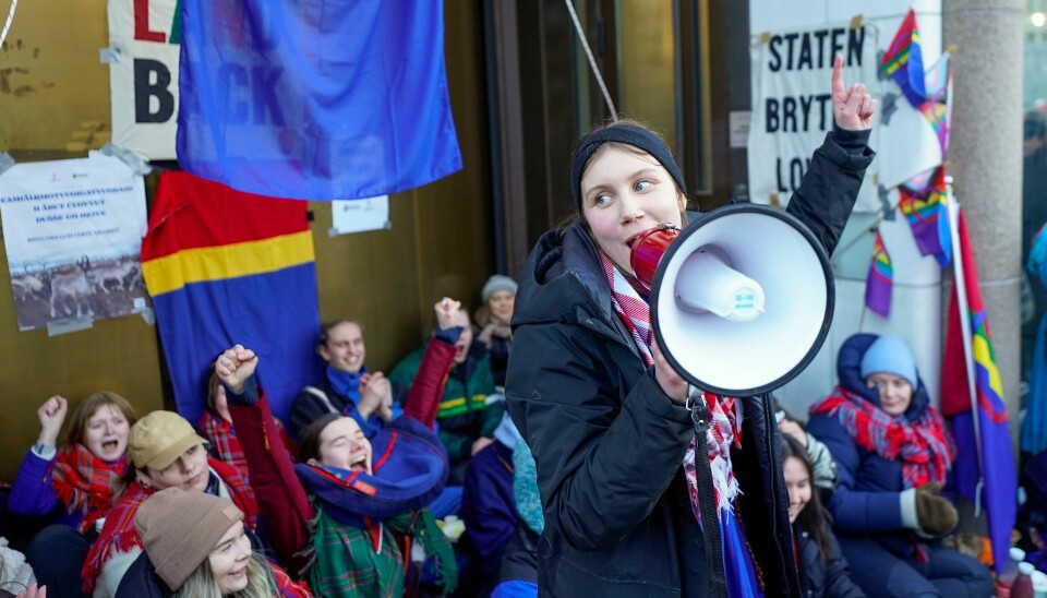 Ella Marie Hætta Isaksen utenfor regjeringskvartalet sammen med aksjonister. I bakgrunnen henger flagget fra «Ellos eatnu - La elva leve»-filmen. Oslo 20230227.