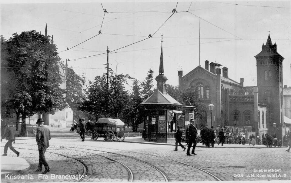 Krysset Karl Johans gate - Kirkegata med Brannvakten, Narvesens tårnkiosk og Domkirkeparken bak. Hest og kjerre, spaserende. Postkort 509. Brannvakta ble oppført i 1854-1856 i tilknytning til Basarene og overlevde så vidt brannen i 1858. Tårnet ble brukt til å tørke brannslanger. Bildet viser krysset Karl Johans gate - Kirkegata med Brannvakta, Narvesens tårnkiosk og Domkirkeparken bak. Domkirken fikk sitt nye tårn i 1850.