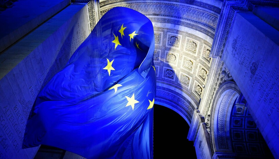 TOPSHOT - A picture shows the European Union flag fluttering under the Arc de Triomphe lit up in blue to mark the French presidency of the European in Paris on January 1, 2022. - France took over the rotating presidency of the EU on January 1, 2022. To mark the start of the six-month EU presidency, historic buildings across the country were illuminated in the blue of the EU flag on New Year's Eve, including the Elysee Palace and the Eiffel Tower. (Photo by JULIEN DE ROSA / AFP)