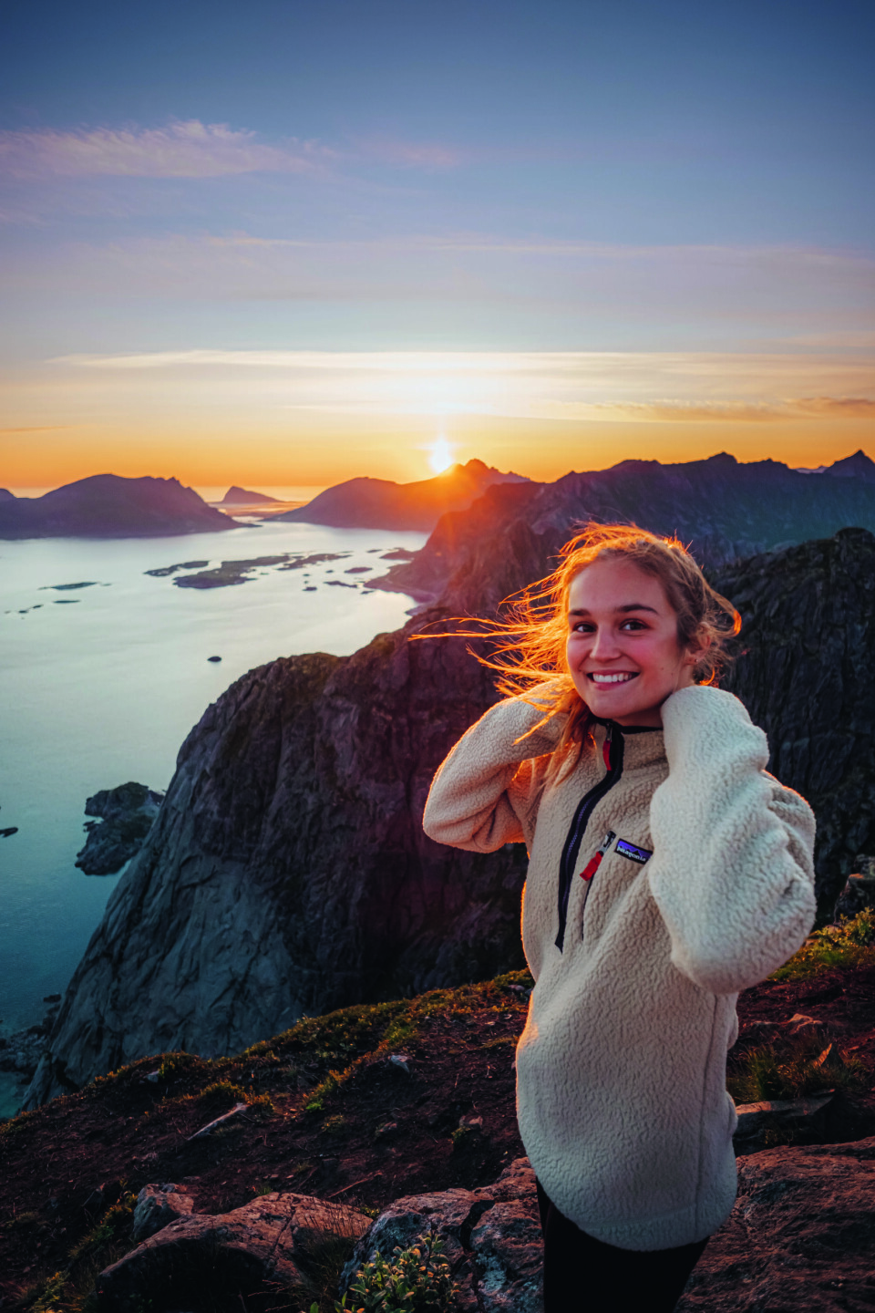 Helene Myhre er aktuell med boken «Tur-retur Norge. På nye eventyr». Jente i 20-årene med brunt hår, iført en hvit ullgenser. Hun står på et fjell med vann og en solnedgang i bakgrunnen.