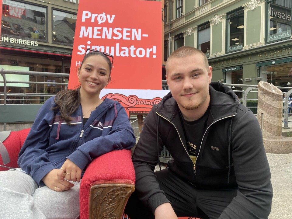 Frida Stølen Sandoval (18) og Silseth (18) prøvde begge mensensimulator. Ti ungdommer foran en plakat.