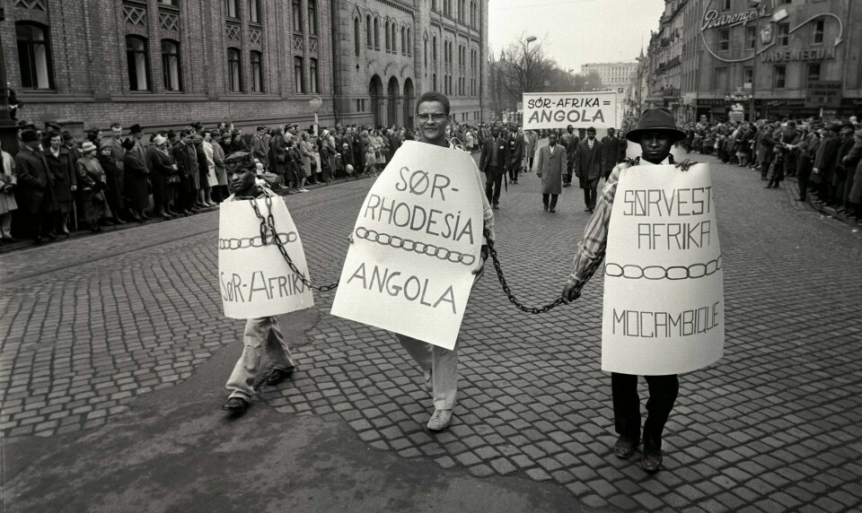 Sør-afrikanske studenter i lenker viser sin avsky mot apartheid 1. mai 1963 på Karl Johans gate. I midten går Hans Beukers med plakaten «Sør-Rhodesia -Angola». Til venstre «Sør-Afrika» og til høyre «Sørvest-Afrika Mocambique». Tre personer går lenket sammen med store plakater, etterfulgt av flere domonstranter.