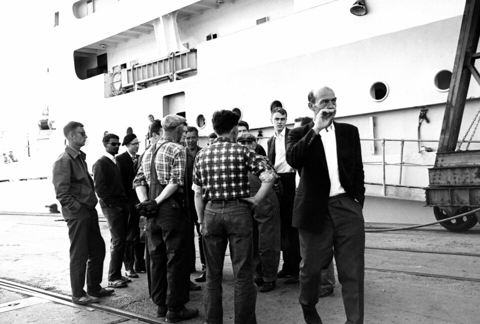Bryggesjauerne på kaia i Oslo ønsket ikke å losse sør-afrikanske varer i juni 1963, men blir tvunget til det da rederiet truer med å gjøre dem erstatningspliktige. Flere menn står samlet på havna.