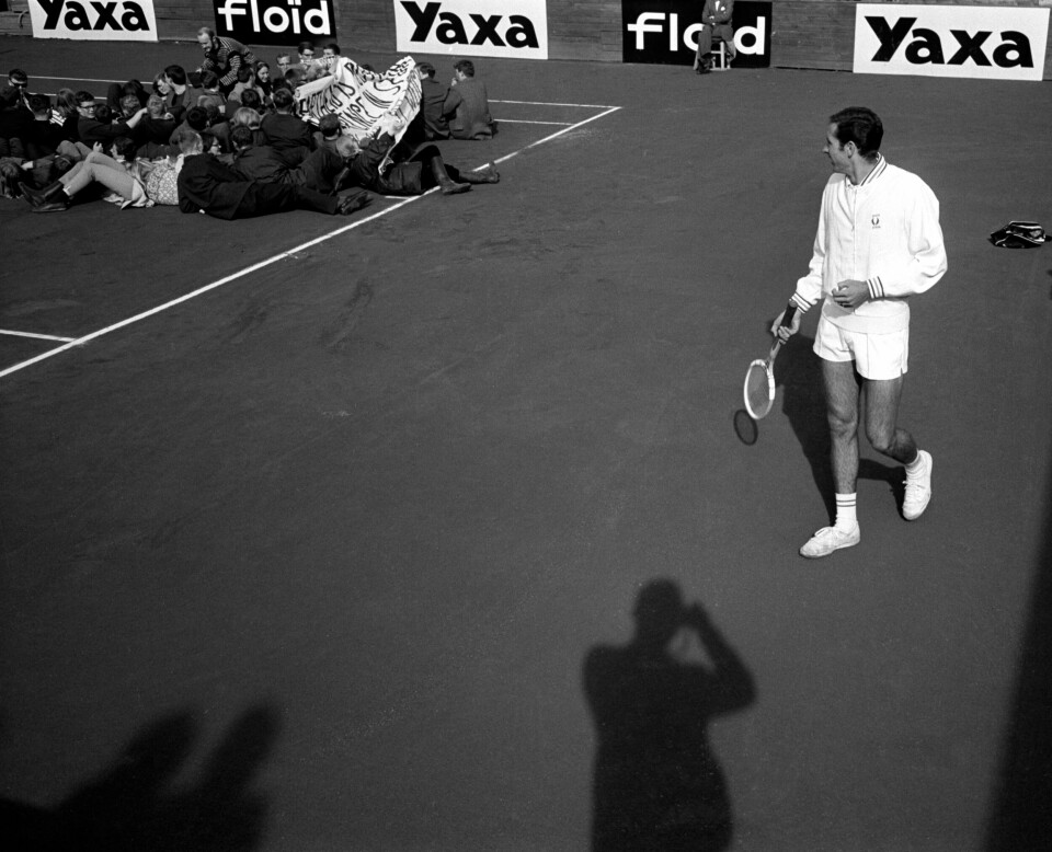 Demonstranter forsøker å hindre tenniskampen mellom Norge og apartheid-regimet Sør-Afrika på Madserud under Davis Cup’en i mai 1964. Sør-Afrika nektet svarte idrettsutøvere å delta. Tennisspiller titter bort på demonstrantene som ligger på banen.
