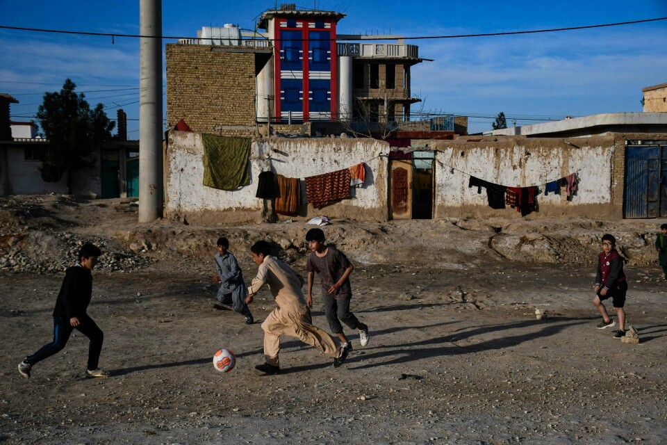 Barn skal leke og spille fotball, ikke gå i krig. Helsesentre, skoler og lekeplasser må prioriteres i krigsområder, mener innleggsforfatter. Unge gutter spiller fotball, i Afghanistan. Bygninger i bakgrunnen, klær henger på en kleshenger over barna.