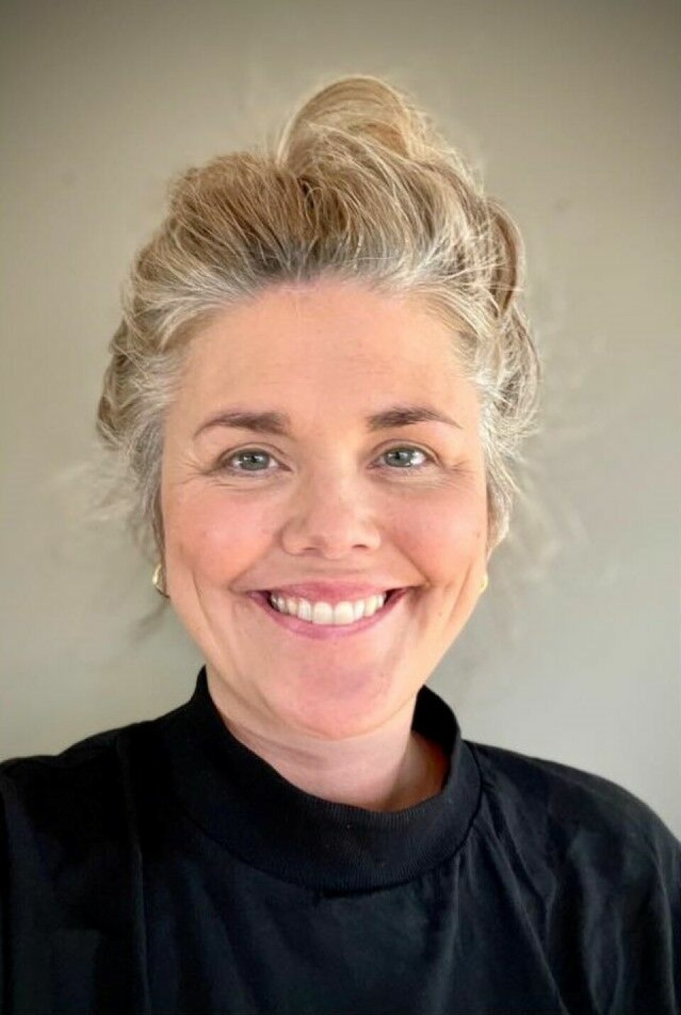 Elin Rise Hvit kvinne med blondt hår, satt opp i en dott. Smiler bredt til kamera.