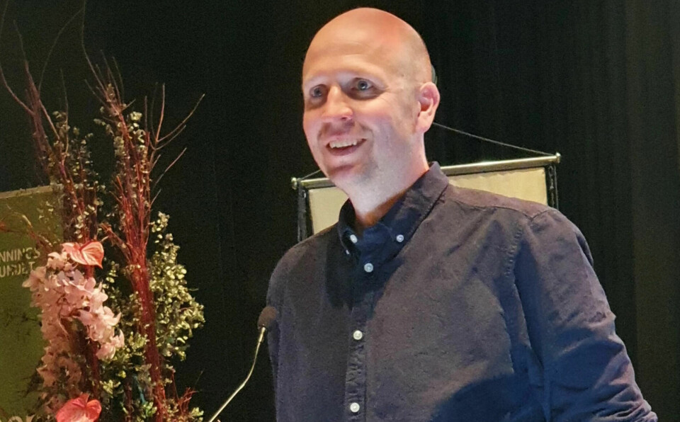 Jo-Gaute Åsgård Mann med skandinavisk utseendet, skallet. Står foran en mikrofon, smiler så man ser tennene. Mørk skjorte på.