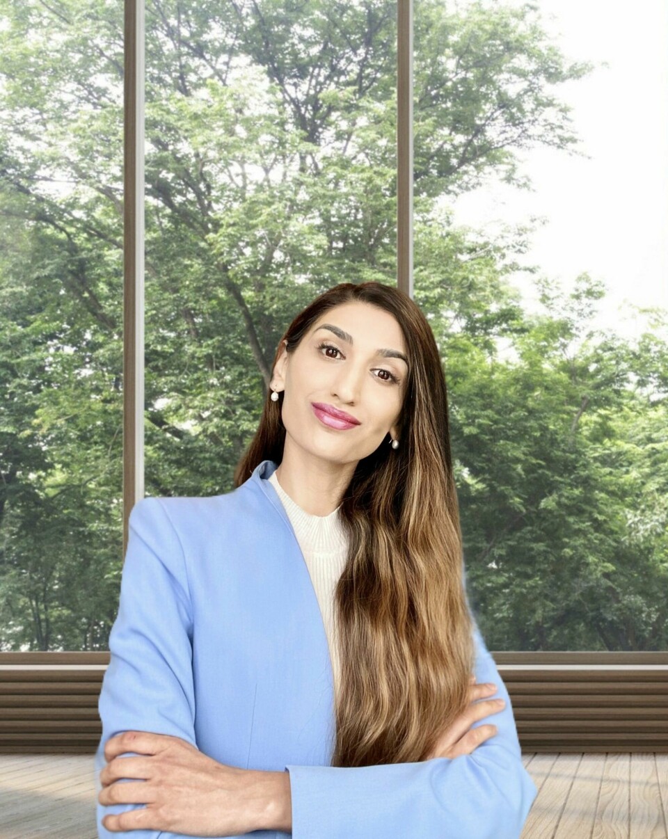Annam Chaudhry Kvinne med pakistansk utseendet, hendene i kors, blå dressjakke. Smiler til kamera, rosa leppestift.