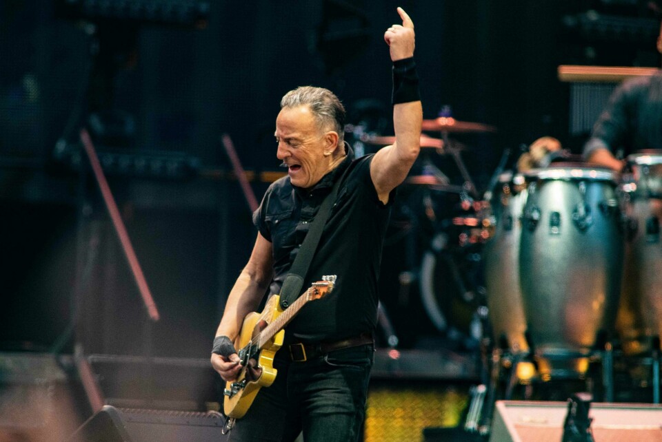 Bruce Springsteen på scenen under en del av Europaturneen. Her i Amsterdam den 25. mai 2023. Bruce Springsteen på scenen under en del av Europaturneen. Her i Amsterdam den 25. mai 2023. Han står med gitar, og spiller med den ene hånda mens han strekker den andre opp i været med pekefingeren opp. Han er kledd i svart, og i bakgrunn kan du så vidt skimte trommene.