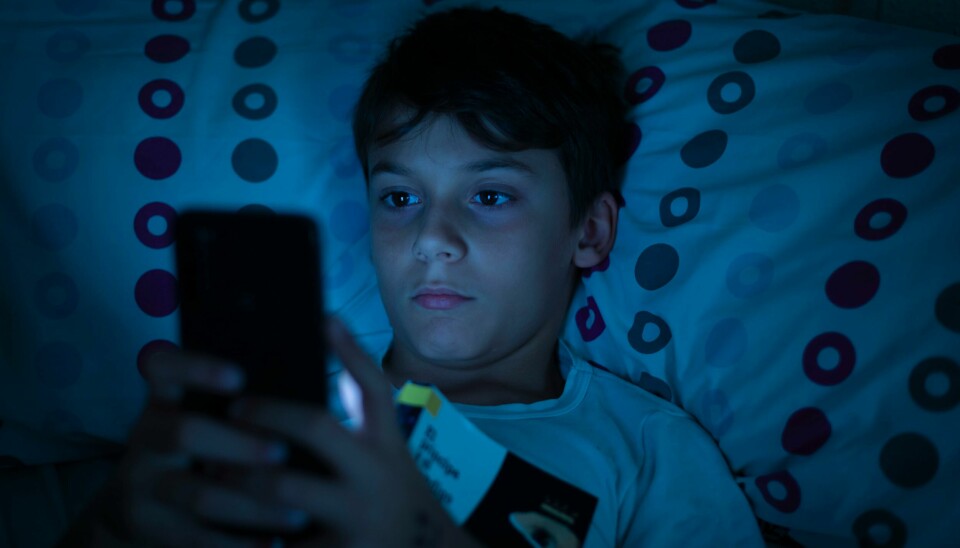 Det er en risiko forbundet med å tillegge chatbotene menneskelige egenskaper. Child in bed at night with a book and a smartphone in the dark. Concept of problems with mobile addiction at young ages. Child with sleeping problems and insomnia due to the use of electronic devices