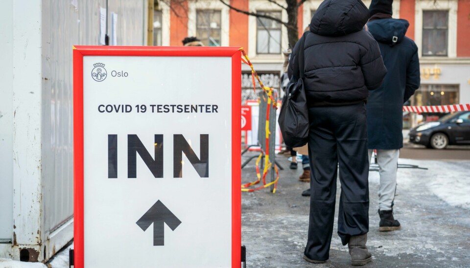 Teststasjonen på Grønland torg i Oslo. Bildet er av folk som står i kø for å få testet seg for korona. Det er is på bakken. Til venstre for dem er det et skilt med pil framover som viser til et senter der folk kan teste seg for smitte. Foto: Ole Berg-Rusten / NTB