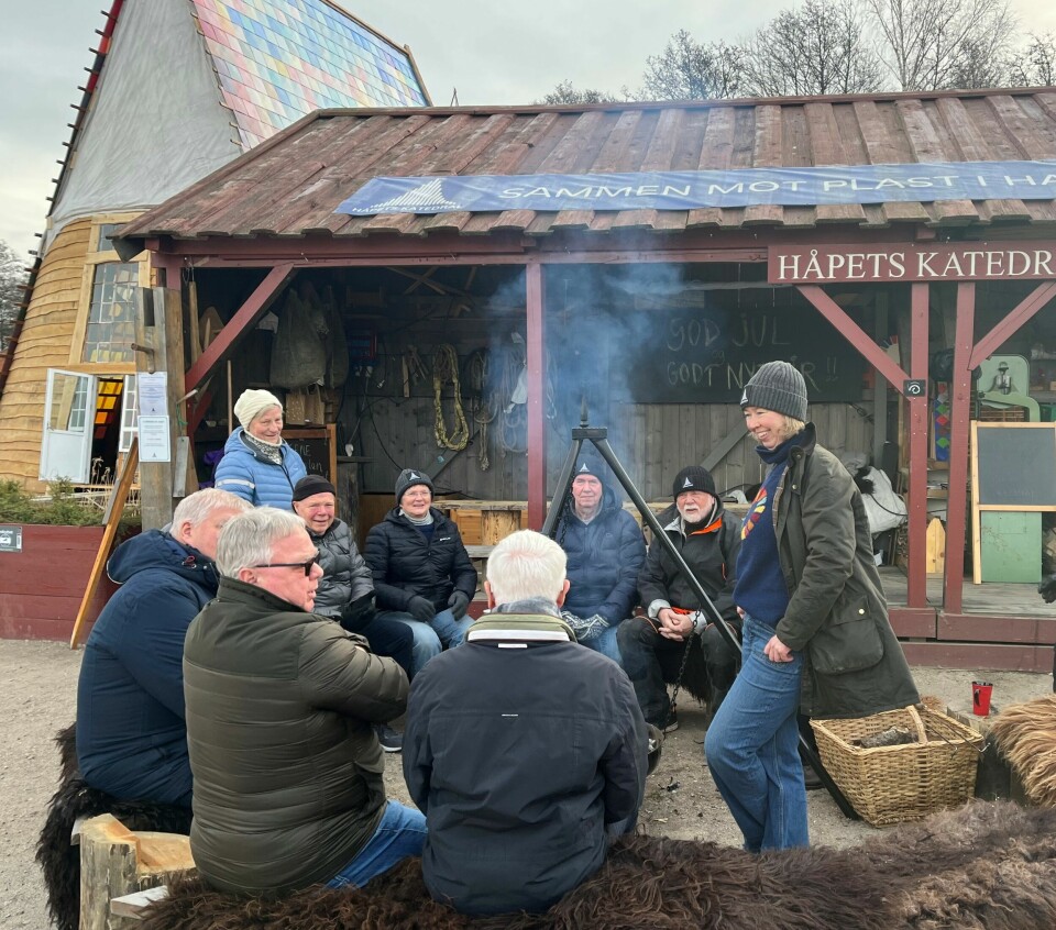 Det var god og lun stemning på Isegran til tross for minusgrader. Solveig Egeland (t.h) småprater med Fredrikstad Bryggeriets Venner rundt bålpanna. Flere menn sitter rundt en bålpanne. Til høyre står en kvinne og smiler