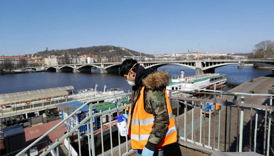 En arbeider sprayer desinfiseringsmiddel på rekkverk langs elven Vltava i Praha.