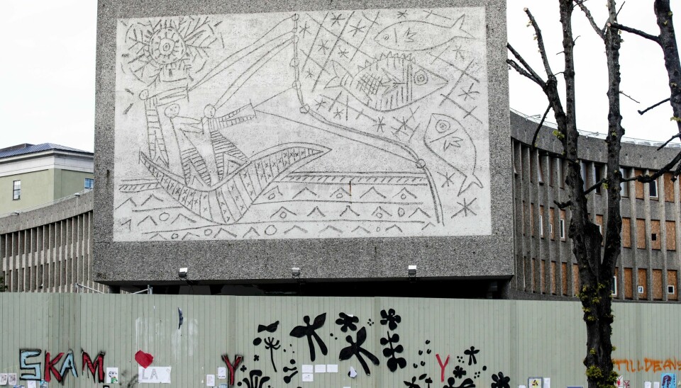 Dersom Y-blokka blir revet, ønsker Larvik kommune å omplassere kunstverket på gavlveggen til kunstner og æresborger Carl Nesjars hjemby. Bildet fra søndag viser plakater på det fire meter høye tregjerdet foran Y-blokka som marker ønsket om å bevare bygningen.