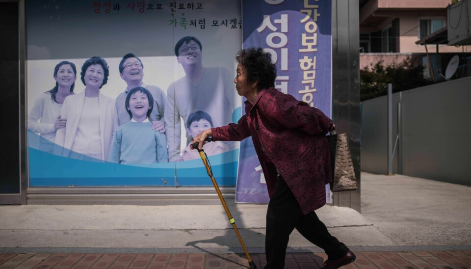 Snart er hver femte innbygger i Sør-Korea 65 år eller eldre. In a photo taken on May 27, 2016 an elderly woman walks past a poster at a health centre in Gunwi, some 200 kilometres south of Seoul.By 2030, a quarter of all South Koreans will be over 65 years old, and the overall population is expected to peak at around 52 million the same year before entering a period of steady decline. This so-called 'silver tsunami' poses a major challenge for Asia's fourth-largest economy as the young, working-age population declines and the cost of caring for the elderly escalates. And in remote, rural communities like Gunwi, which lies some 200 kilometers southeast of Seoul, the trend is exacerbated by a youth exodus to the cities for work. / AFP PHOTO / Ed Jones / TO GO WITH AFP STORY SKOREA-SOCIETY-EDUCATION-POPULATION-AGING,FEATURE BY JUNG HA-WON