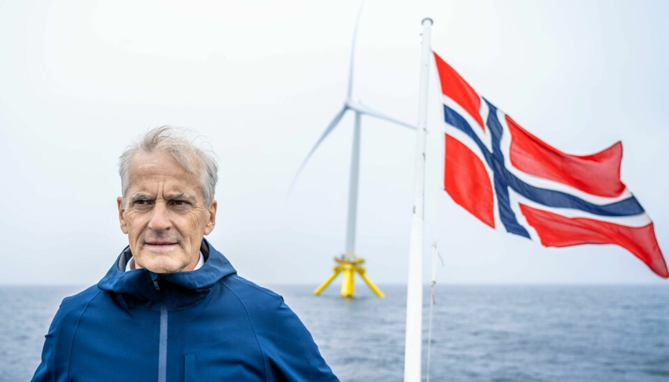 Regjeringens havvindssatsning har kun ført til ulemper, skriver innleggsforfatter. Mann med grått hår, skandinavisk hvit hud, blå regnjakke, vedwsiden av flagrende norskeflagg og en hav vindmølle i havet bak han.