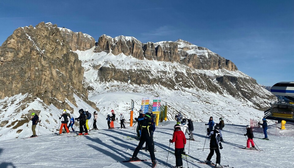 På rundt 2.500 meter over havet venter skiturister på å kjøre ned bakkene fra Passo Pordoi i Val di Fassa. Mennesker står på toppen av slalåmbakken med Dolomittene i bakgrunnen.