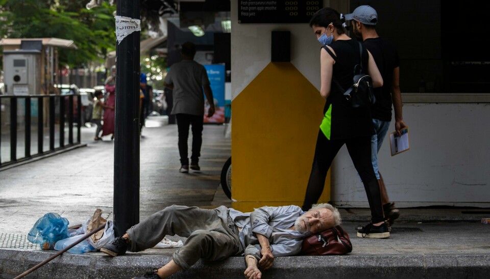 Folk går forbi en hjemløs mann som sover på gaten i Beirut i Libanon. Folk går forbi en hjemløs mann som sover på gaten i Beirut i Libanon. Foto: Hassan Ammar / AP / NTB