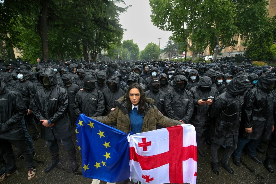 Opposisjonelle til loven i Georgia frykter at den vil sette en stopper for et mulig EU-medlemskap. Her demonstrerer en kvinne i Tbilisi foran opprørspoliti samme dag som loven ble vedtatt. A woman holds a Georgian national and an EU flags in front of riot police blocking a street to prevent demonstrators during an opposition protest against 'the Russian law' near the Parliament building in the center of Tbilisi, Georgia, Tuesday, May 14, 2024. The Georgian parliament on Tuesday approved in the third and final reading a divisive bill that sparked weeks of mass protests, with critics seeing it as a threat to democratic freedoms and the country's aspirations to join the European Union. (AP Photo/Zurab Tsertsvadze)