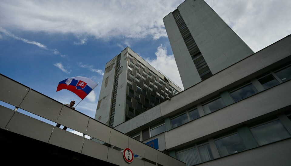Slovakias statsminister Robert Fico, som ble skutt og såret onsdag, ligger fortsatt på intensivavdeling og er igjen blitt operert. En mann med et slovakiske flagget ved sykehuset der Fico er innlagt. Foto: Denes Erdos / AP / NTB