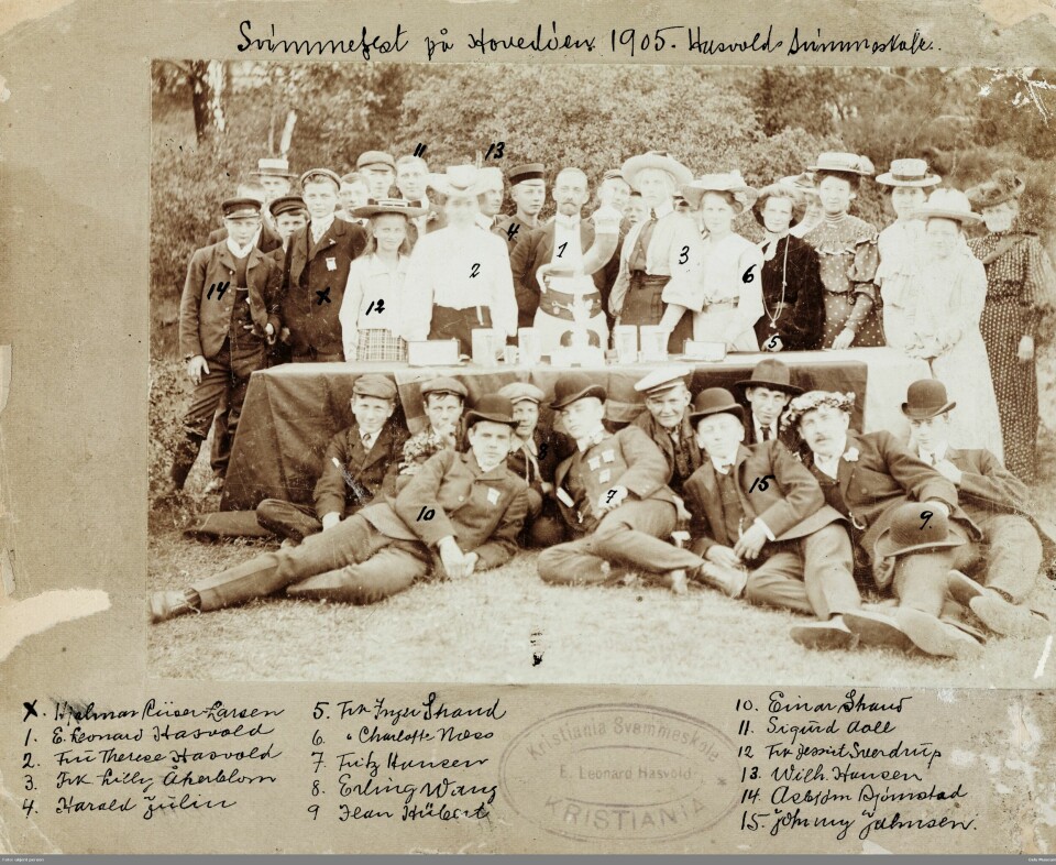 Hasvolds svømme- og livredningsskole har svømmefest på Hovedøya 1905. Avbildete personer: Einar Strand, Sigurd Aall, Asbjørn Bjørnstad, Fritz Hansen, Wilhelm Hansen, Edvard Leonard Hasvold, Therese Hasvold, Jeans Hübert, Johnny Johnsen, Harald Julin, Charlotte Næss, Hjalmar Riiser-Larsen, Inger Strand, Erling Wang og Lilly Åkerblom. Pyntede damer og menn med hatter står bak et bord. Foran bordet sitter flere menn.
