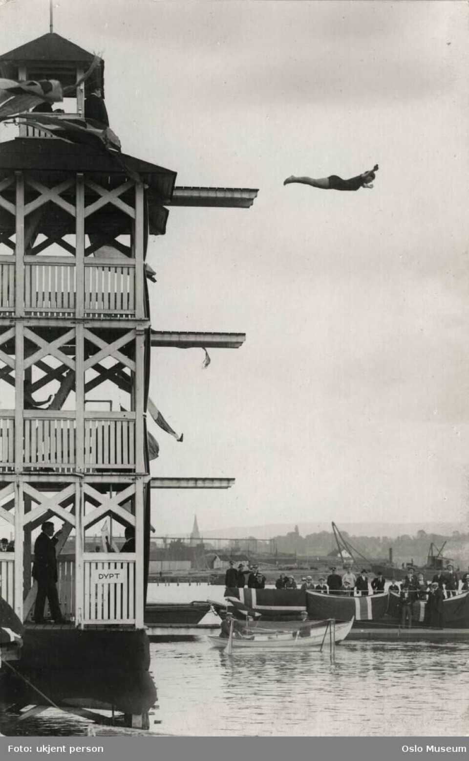 Kvinne i fritt stup fra badetårnet på Hasvolds bad ca. 1905. Det er fire stupebrett i høyden. Kvinnen hopper fra det øverste.