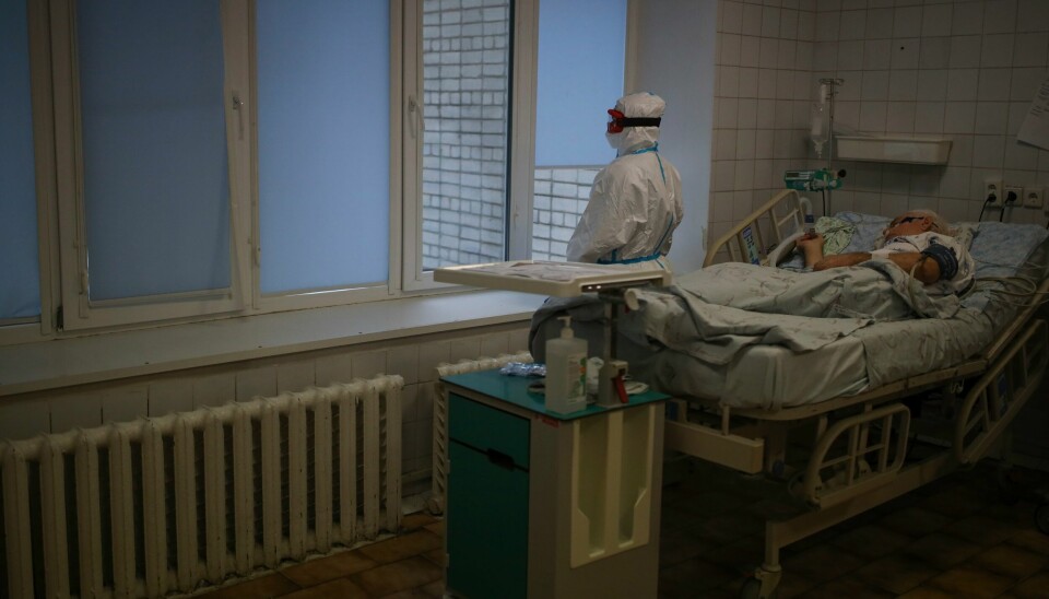 Helsepersonell står ved siden av en pasient med COVID-19 på en intensivavdeling ved et sykehus i Krasnodar, sør i Russland i 2022. En russisk helsearbeider kikker ut av vinduet ved siden av en koronapasient på en intensivavdeling i Krasnodar i Russland. Foto: Vitaliy Timkiv / AP / NTB