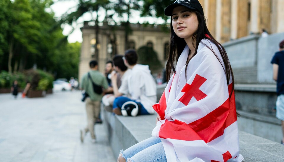 Lizi (17) er tydelig på at hun protesterer mot russisk påvirkning på hjemlandet. - Det er svært farlig, sier 17 år gamle Lizi Qatamadze, som sitter på trappa med et georgisk flagg rundt koppen.