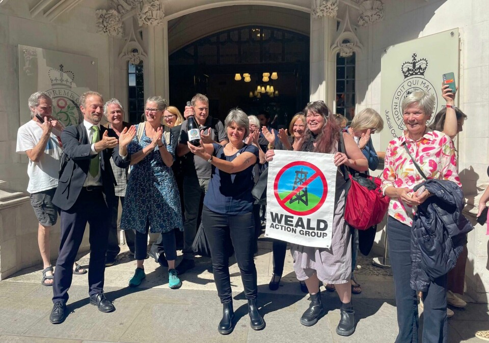Oljemotstander Sarah Finch feirer med sine tilhengere etter seieren i britisk rett der en konsesjon ble underkjent. Environmental campaigner Sarah Finch, center, celebrates outside the Supreme Court in London, Thursday June 20, 2024 after justices ruled that emissions generated from burning fuel should be considered when granting planning permission for oil sites. The 3-2 ruling Thursday in London was a victory for fossil fuel opponents. (Callum Parke/PA via AP)