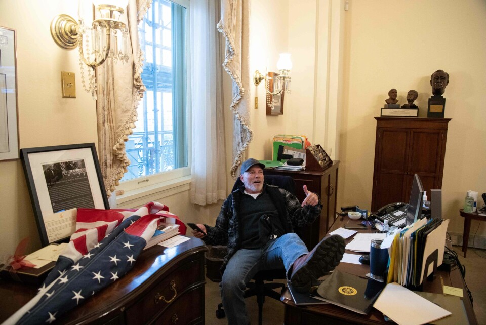 En av dem som deltok i Kongresstormingen 6. januar i fjor sitter ved pulten til toppdemokraten Nancy Pelosi. En av dem som deltok i Kongresstormingen 6. januar i fjor sitter ved pulten til toppdemokraten Nancy Pelosi.