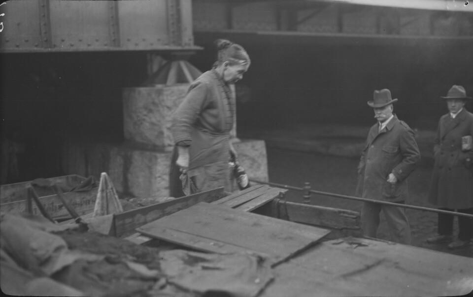 En kvinne på sin husbåt på Akerselva en gang mellom 1915 til 1940. Sort hvitt bilde av kvinnen på båten med to menn stående til høyre på land ved båten