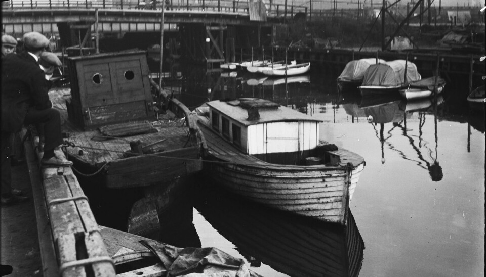 Husbåter på elva i 1934. Jernbanetollbygningen i bakgrunnen. Husbåter på elva. Vi ser Jernbanetollbygningen i bakgrunnen.