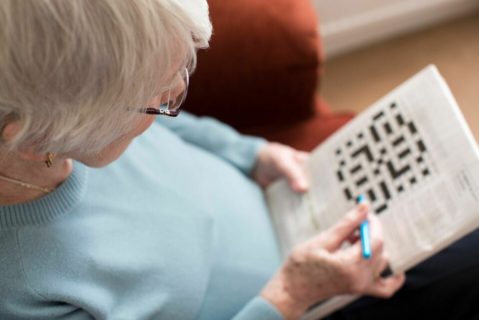 Har du spørsmål eller bekymringer knyttet til demens? Ta kontakt med Demenslinjen, 23 12 00 40. Seniorkvinne gjør kryssord hjemme.