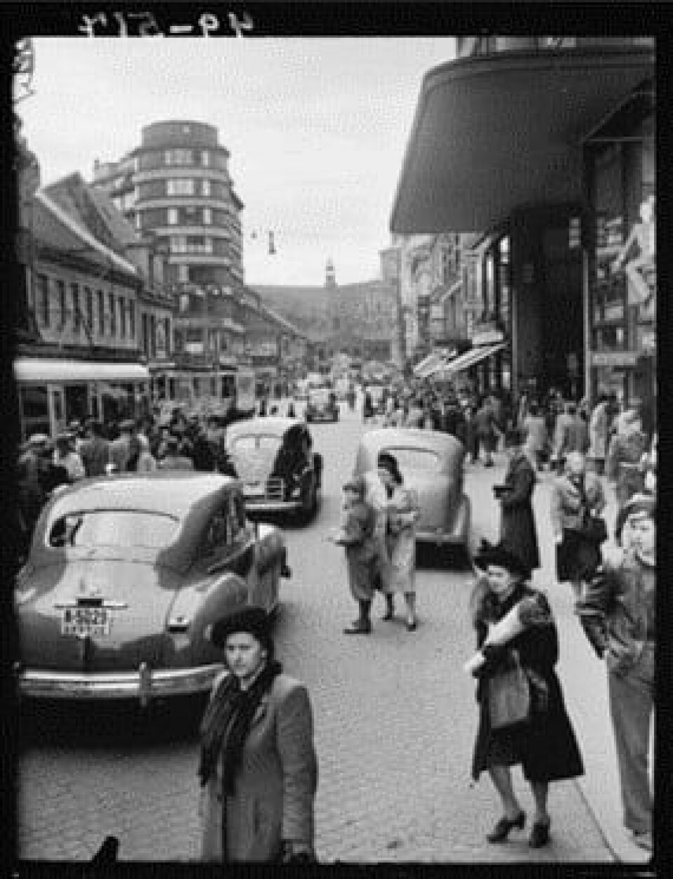 Storgata var lenge en av byens farligste gater. Kombinasjonen av bil, trikk, hest og mengder av fotgjengere kunne bli dødelig. Særlig foran Gunerius var det mange ulykker. Dette bildet er fra 1949. Det er fullt av fotgjengere på fortauene. Flere fotgjengere krysser gata flere steder. Flere biler kjører i gata.