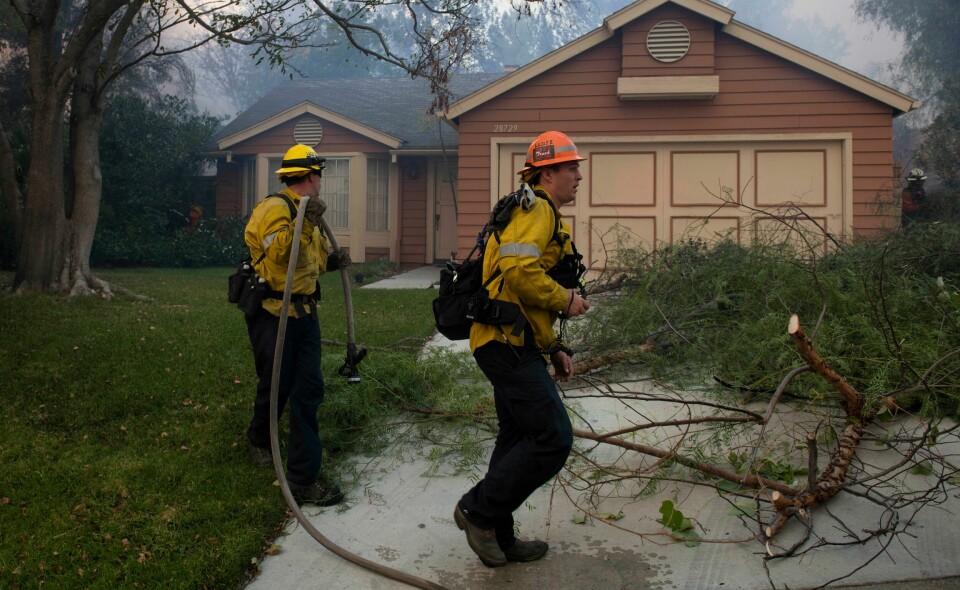 En skogbrann truer med å ødelegge dette huset i Santa Clarita i California. Myndighetene vet ikke hvor mange hus som er ødelagt i brannene flere steder i delstaten. Firefighters rush to protect a home as the flames of the Tick Fire approach behind it Thursday, Oct. 24, 2019, in Santa Clarita, Calif. Fast-growing fires across California have forced thousands of people to evacuate as dry winds and high heat feed the flames. (AP Photo/ Christian Monterrosa)