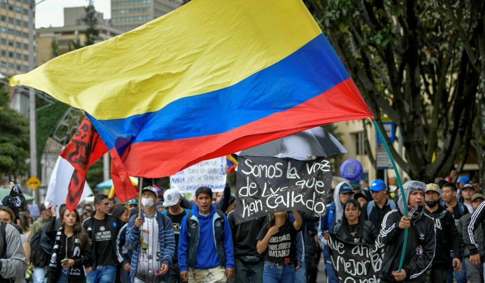 Demonstranter med et colombiansk flagg i en markering mot regjeringen til president Ivan Duque under onsdagens streik i Bogota. På den ene plakaten står det «Vi er stemmen til dem de har stilnet». Foto: Raul Arboleda/NTB scanpix