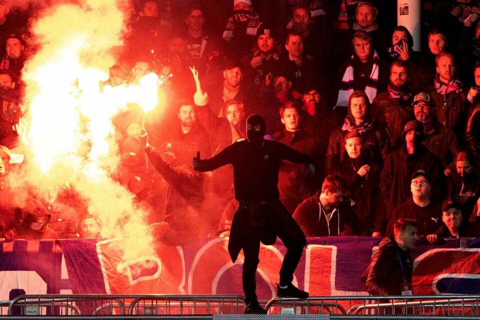 En maskert vålerengasupporter står foran Klanen som brenner bluss under eliteseriekampen mellom Lillestrøm og Vålerenga på Åråsen 26. oktober. Nå er begge klubbene bøtelagt.