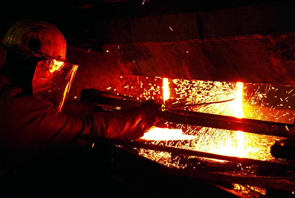 Fra stålsmelteverket i Mo i Rana. Metallskrot smeltes om til stål. En arbeider renser opp i det flytende stålet, slik at strømmen ikke skal bli ujevn. Har på seg vernehjelm. Industri.