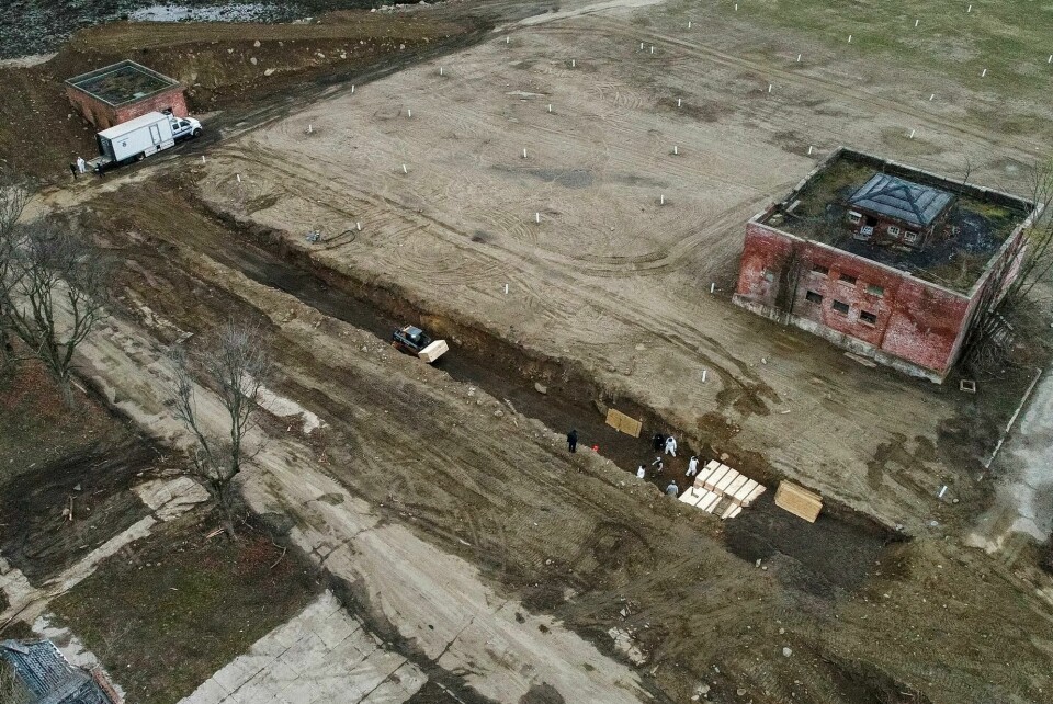 Arbeidere med beskyttelsesutstyr begraver døde personer på Hart Island i Bronx, New York. Bildet er tatt i april. Workers wearing personal protective equipment bury bodies in a trench on Hart Island in the Bronx borough of New York on April 9, 2020. Hart Island is a strip of land in Long Island Sound that has long served as the city's potter's field. (AP Photo/John Minchillo)