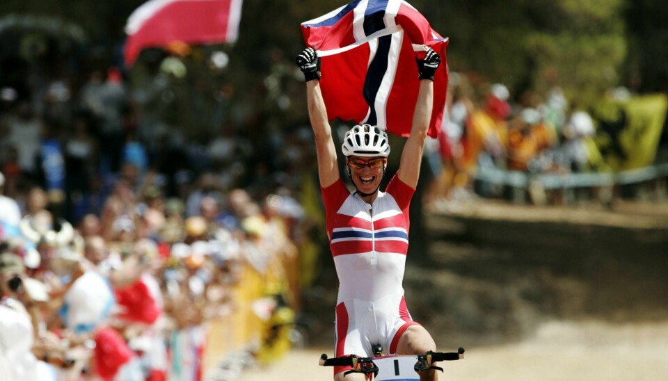 Aten, Hellas 20040827. OL / Olympiske Leker i Aten 2004. Terrengsykling, kvinner.
Gunn-Rita Dahle jubler med det norske flagget over hodet i det hun sykler i mål som OL vinner i terrengsykling for damer i Aten.
Foto: Cornelius Poppe / NTB