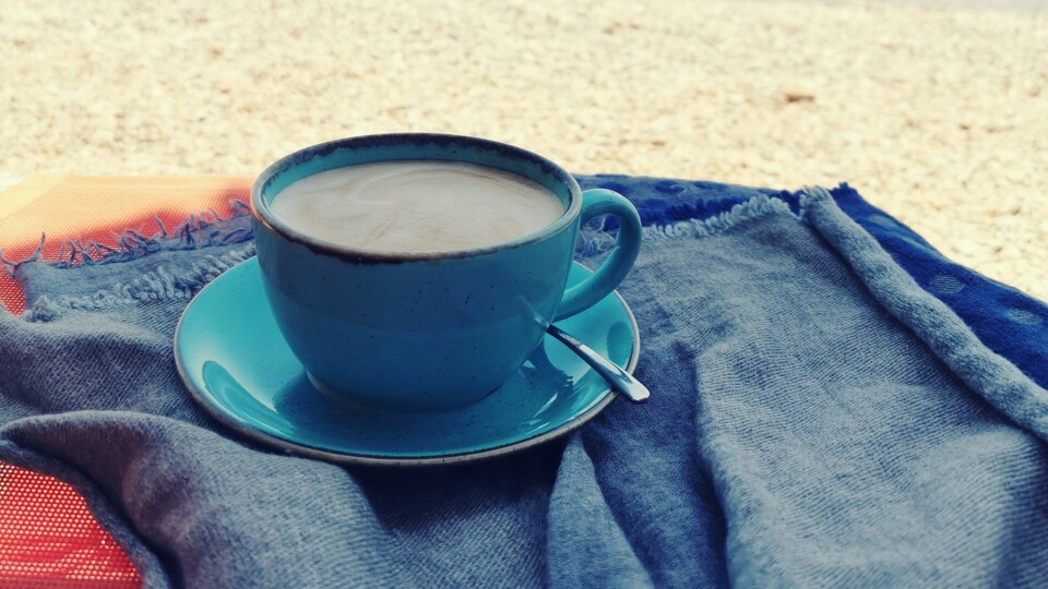 Hege Rørvik ble årets første ukesvinner i Demokratens Fotosommer. Kaffekopp på pledd ved en strand.