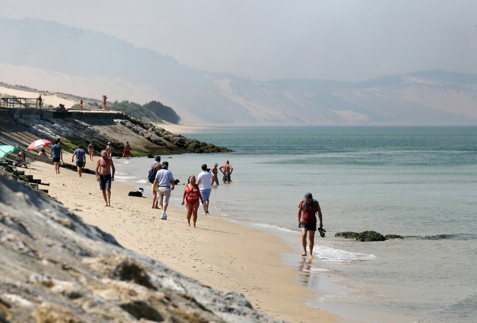 Det ble registrert varmerekorder flere steder i Frankrike mandag. Her går folk på stranden i regionen Nouvelle-Aquitaine sørvest i landet Folk rusler langs stranden i Sørvest-Frankrike mandag. Foto: Bob Edme / AP / NTB