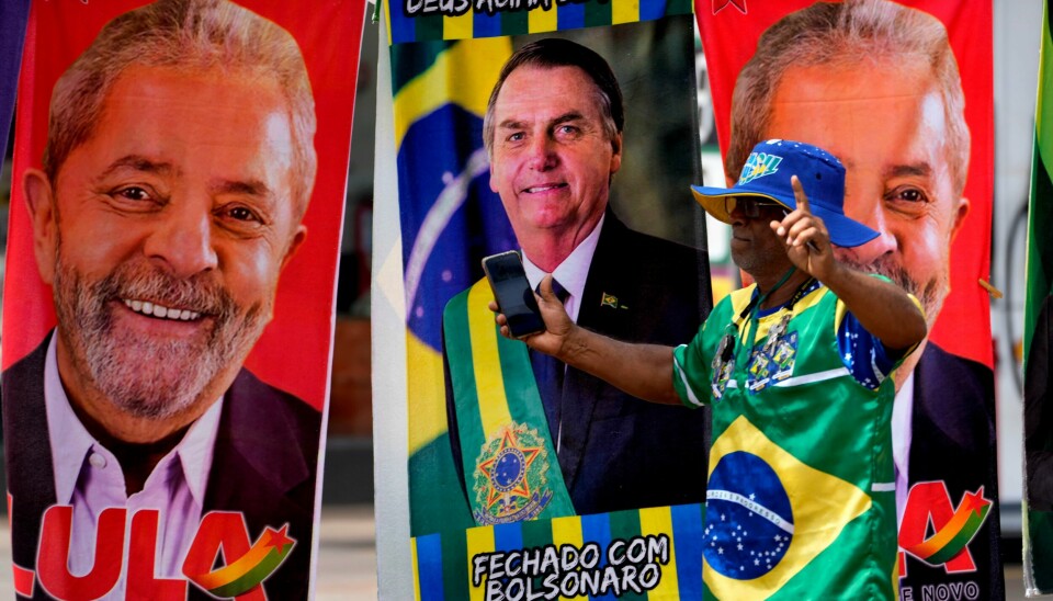 Søndag 2. oktober holdes første valgomgang i det brasilianske presidentvalget. Luiz Inacio «Lula» da Silva (t.v.) kan allerede da sikre seieren over sittende president Jair Bolsonaro (midten). En mann går foran håndklær med bilde av presidentkandidatene Luiz Inacio «Lula» da Silva og Jair Bolsonaro.